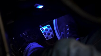 Close-up of a man in summer shoes presses the brake pedal in the car, slow motion. Footage. Sport car driver push clutch pedal in blue lights on night.