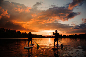 rear view of two people on sup boards which floating on the river at sunset