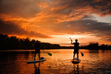 Beautiful rear view of two people on sup boards which floating on the river at sunset