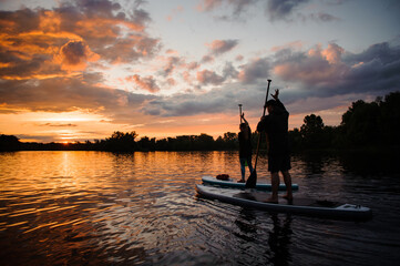 Couple of people on sup boards floating on the river at sunset