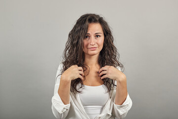 Pointing with hand at chest and staring. Shocked facial expression. Young attractive woman, dressed white blouse, with brown eyes, curly hair, yellow background