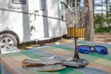 On the table is a glass of beer, stockfish, sunglasses.
Blurred caravan background.
Concept: outdoor recreation