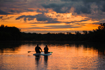 romantic rear view on couple of sitting people on sup boards on the river at sunset