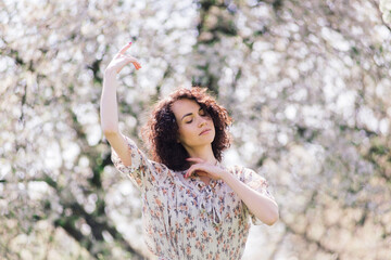 Young attractive woman with curly long hair posing in spring blooming garden, apple trees