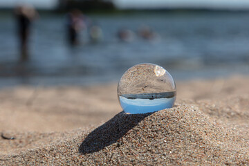 glass ball on the sand.
   Inverted view of the sea and coast in Finland. People swimming in the sea.