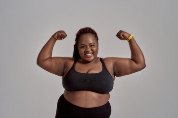 Enjoy your body. Plump, plus size african american woman in sportswear smiling at camera, showing...