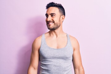 Young handsome man with beard wearing casual sleeveless t-shirt over pink background looking to side, relax profile pose with natural face and confident smile.