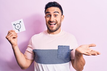 Young handsome man with beard asking for equality holding paper with transgender symbol celebrating achievement with happy smile and winner expression with raised hand