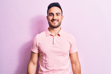 Young handsome man with beard wearing casual polo standing over pink background with a happy and...