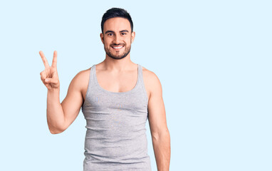 Naklejka premium Young handsome man wearing swimwear and sleeveless t-shirt showing and pointing up with fingers number two while smiling confident and happy.