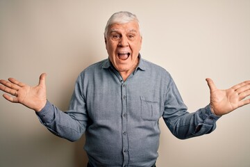 Naklejka premium Senior handsome hoary man wearing casual shirt standing over isolated white background celebrating crazy and amazed for success with arms raised and open eyes screaming excited. Winner concept