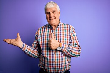 Naklejka premium Senior handsome hoary man wearing casual colorful shirt over isolated purple background Showing palm hand and doing ok gesture with thumbs up, smiling happy and cheerful