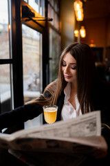Beautiful woman with brunette hair in dark clothes looking at window and drinking orange hot drink. Concept of cozy places and cold winter. Concept of cafe and coffee shop. Cosy and atmosphere place.
