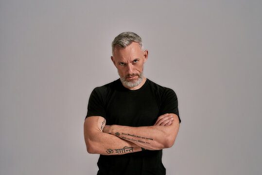 Strength. Middle Aged Man With Crossed Arms In Black T Shirt Looking At Camera While Posing In Studio Over Grey Background