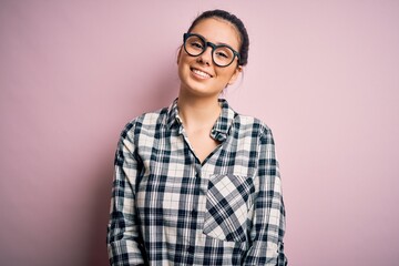 Young beautiful brunette woman wearing casual shirt and glasses over pink background with a happy and cool smile on face. Lucky person.