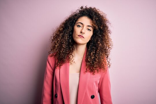 Young beautiful businesswoman with curly hair and piercing wearing elegant jacket looking sleepy and tired, exhausted for fatigue and hangover, lazy eyes in the morning.