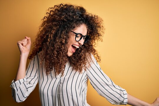 Young beautiful woman with curly hair and piercing wearing striped shirt and glasses Dancing happy and cheerful, smiling moving casual and confident listening to music
