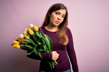 Young blonde woman holding romantic bouquet of yellow tulips flowers over pink background looking sleepy and tired, exhausted for fatigue and hangover, lazy eyes in the morning.