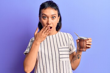 Young woman drinking mate infusion covering mouth with hand, shocked and afraid for mistake....