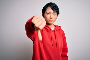 Young beautiful asian girl wearing casual sweatshirt with hoodie over white background looking unhappy and angry showing rejection and negative with thumbs down gesture. Bad expression.