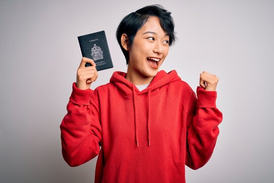 Young beautiful chinese tourist woman on vacation holding canada canadian passport pointing and showing with thumb up to the side with happy face smiling