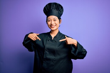 Young beautiful chinese chef woman wearing cooker uniform and hat over purple background looking confident with smile on face, pointing oneself with fingers proud and happy.