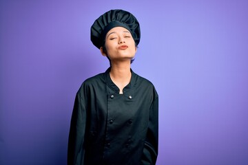 Young beautiful chinese chef woman wearing cooker uniform and hat over purple background looking at the camera blowing a kiss on air being lovely and sexy. Love expression.