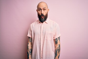 Handsome bald man with beard and tattoo wearing casual shirt over isolated pink background afraid and shocked with surprise expression, fear and excited face.