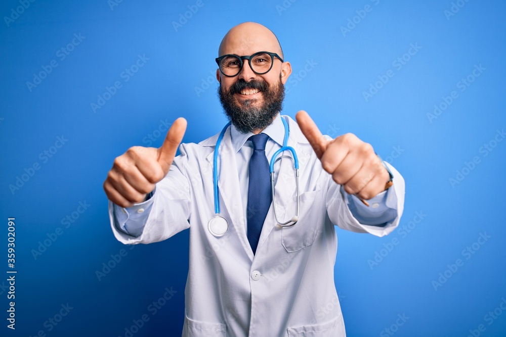 Poster Handsome bald doctor man with beard wearing glasses and stethoscope over blue background approving doing positive gesture with hand, thumbs up smiling and happy for success. Winner gesture.