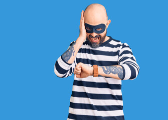Young handsome man wearing burglar mask looking at the watch time worried, afraid of getting late