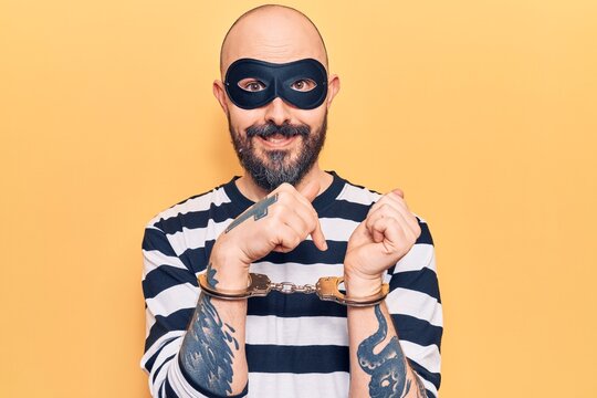 Young handsome man wearing burglar mask and handcuffs smiling happy pointing with hand and finger