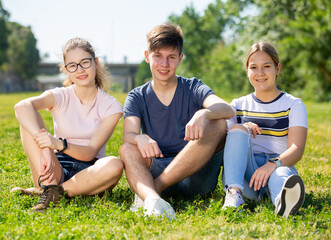 Cheerful teen friends sitting together on green lawn