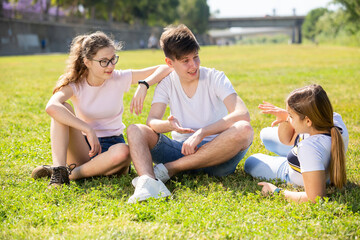 Cheerful teen boy and girls talking on green lawn