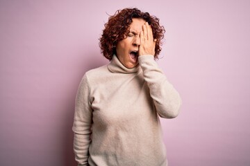 Middle age beautiful curly hair woman wearing casual turtleneck sweater over pink background Yawning tired covering half face, eye and mouth with hand. Face hurts in pain.