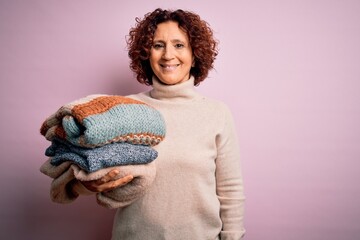 Middle age curly hair housework woman holding pile of clothes over isolated pink background with a happy face standing and smiling with a confident smile showing teeth