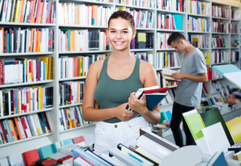teenage girl holding new books pile in shop