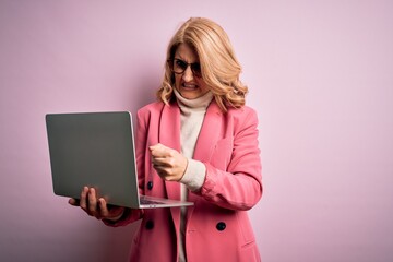 Middle age beautiful blonde business woman working using laptop over pink background annoyed and frustrated shouting with anger, crazy and yelling with raised hand, anger concept