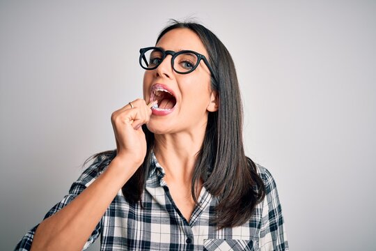 Young caucasian woman wearing glasses brushing her teeth using tooth brush and oral paste, cleaning teeth and tongue as healthy health care morning routine