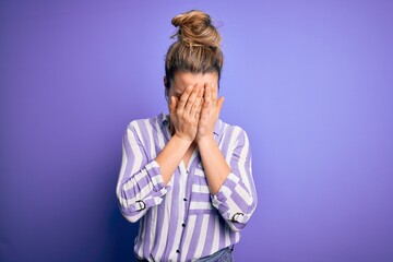 Young beautiful blonde woman wearing casual striped shirt standing over purple background with sad expression covering face with hands while crying. Depression concept.
