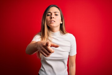 Obraz premium Beautiful blonde woman with blue eyes wearing casual white t-shirt over red background pointing displeased and frustrated to the camera, angry and furious with you