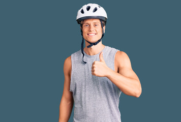 Young handsome man wearing bike helmet doing happy thumbs up gesture with hand. approving expression looking at the camera showing success.