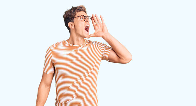 Young handsome man wearing casual clothes and glasses shouting and screaming loud to side with hand on mouth. communication concept.