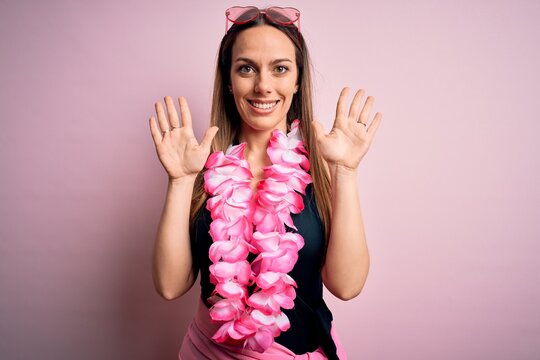 Young beautiful blonde woman wearing swimsuit and floral Hawaiian lei over pink background showing and pointing up with fingers number ten while smiling confident and happy.