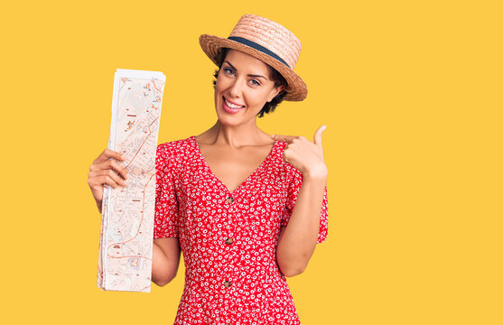 Young beautiful woman wearing summer hat holding map pointing finger to one self smiling happy and proud