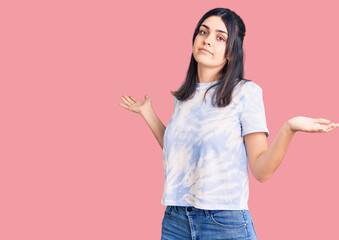 Young beautiful girl wearing casual t shirt clueless and confused expression with arms and hands...