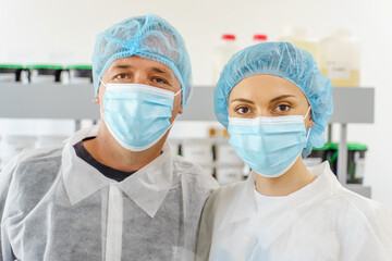 Two caucasian doctors or scientists at hospital or laboratory - Man and woman people wearing protective equipment mask and bouffant cap looking to the camera - protection and solution concept
