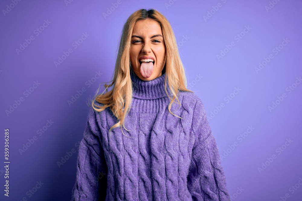 Sticker young beautiful blonde woman wearing casual turtleneck sweater over purple background sticking tongu