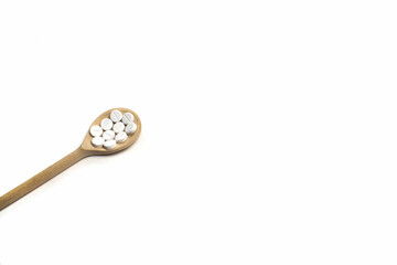 Wooden spoon with round white tablets on a white background isolated on the left side. Medications on the table for coronavirus and pandemic, close up. Free space for text. Pills and drugs. Top view