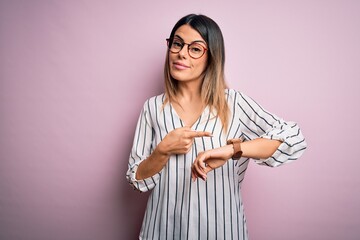 Young beautiful woman wearing casual striped t-shirt and glasses over pink background In hurry...