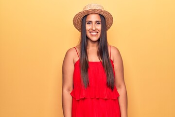 Young beautiful brunette woman wearing summer hat and dress looking positive and happy standing and smiling with a confident smile showing teeth